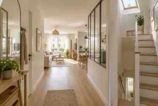 Intérieur lumineux d’une maison mitoyenne étroite avec verrière, escalier éclairé par une fenêtre de toit et murs clairs.